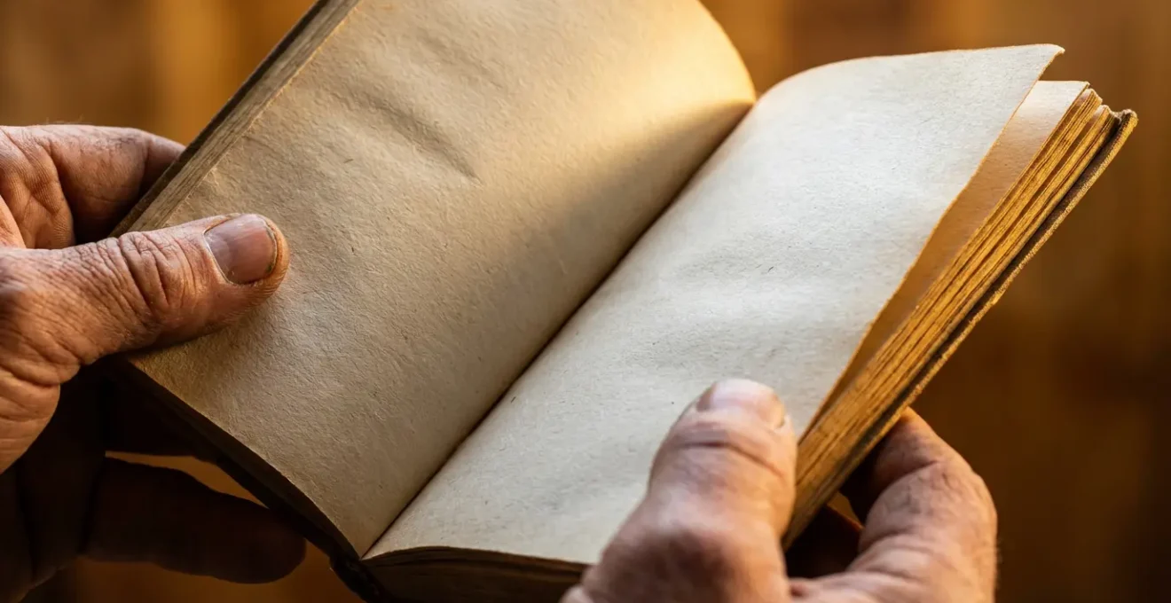 Gros plan macro d'une main tenant délicatement un recueil de poésie ouvert, avec les mots flous et la texture du papier visible en détail